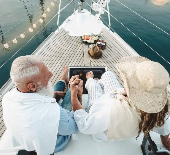 Senior couple celebrating wedding anniversary on sailboat - Happy mature people having fun on boat trip vacation - Love relationship and travel elderly people lifestyle concept
